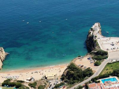 Vista aérea de una playa con agua turquesa, arena y rocas, rodeada de edificios.