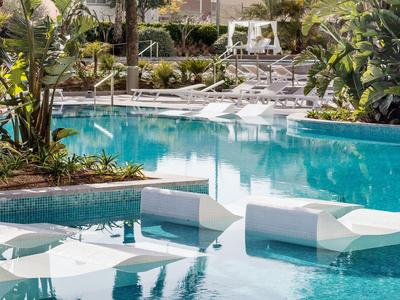 Moderner Poolbereich mit weißen Sitzmöbeln und umgeben von Pflanzen in einem Hotel.