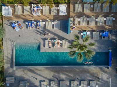 Luftaufnahme eines rechteckigen Pools mit Sonnenschirmen und Liegestühlen neben einem Hotel.