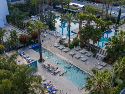 Blick auf Hotelpool mit Liegen, Palmen und Sonnenschirmen in tropischer Anlage.