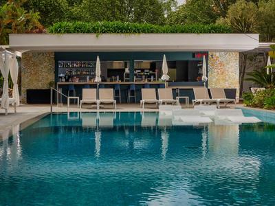Moderner Poolbereich mit Liegestühlen und Bar in tropischer Hotelumgebung.