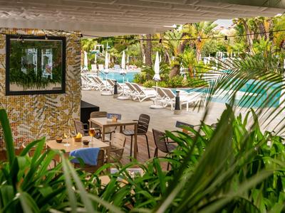 Überdachter Essbereich mit Tisch und Stühlen, Blick auf Pool und Liegestühle im Urlaubshotel.