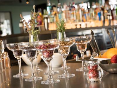 Varios vasos llenos de diferentes frutas en una barra con botellas al fondo.