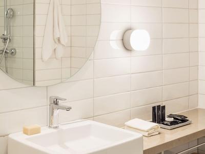 Modernes Badezimmer mit rundem Spiegel, Waschbecken, Wandlampe und Handtüchern unter dem Waschbecken.