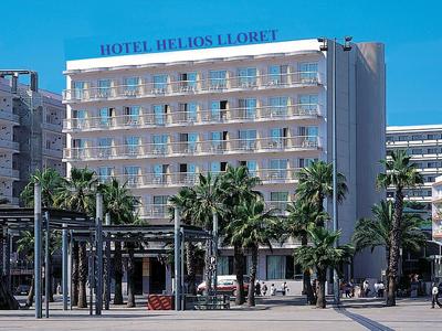 Modern hotel Helios Lloret met balkons en palmbomen ervoor onder een heldere blauwe lucht