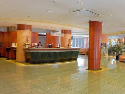 Ruime hotel lobby met receptie, zithoek en warme verlichting.