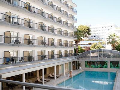 Modern hotel met balkons, buitenzwembad, ligstoelen en heldere blauwe lucht.