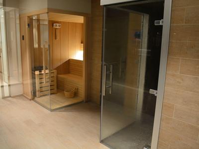 Spa-ruimte met houten sauna en glazen stoomcabine in een moderne, beige betegelde omgeving.