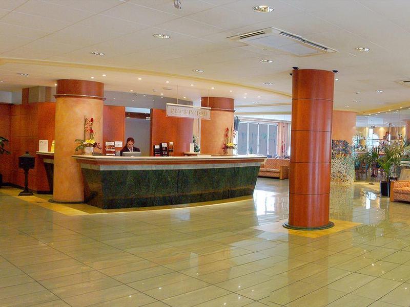 Ruime hotel lobby met receptie, zithoek en warme verlichting.