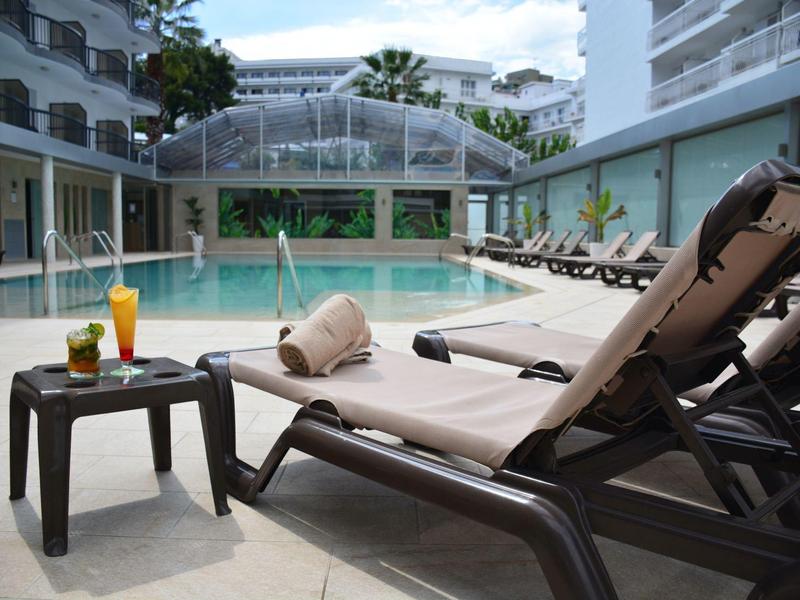 Ligstoelen met handdoeken en drankjes bij een hotelzwembad onder een gedeeltelijk bewolkte hemel.