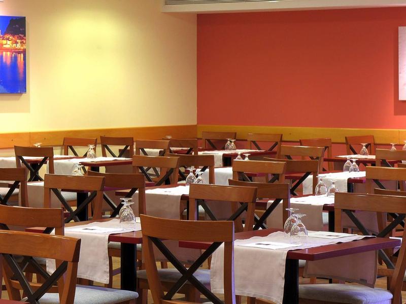 Lege eetruimte met houten stoelen, witte tafelkleden en rode en gele muren.