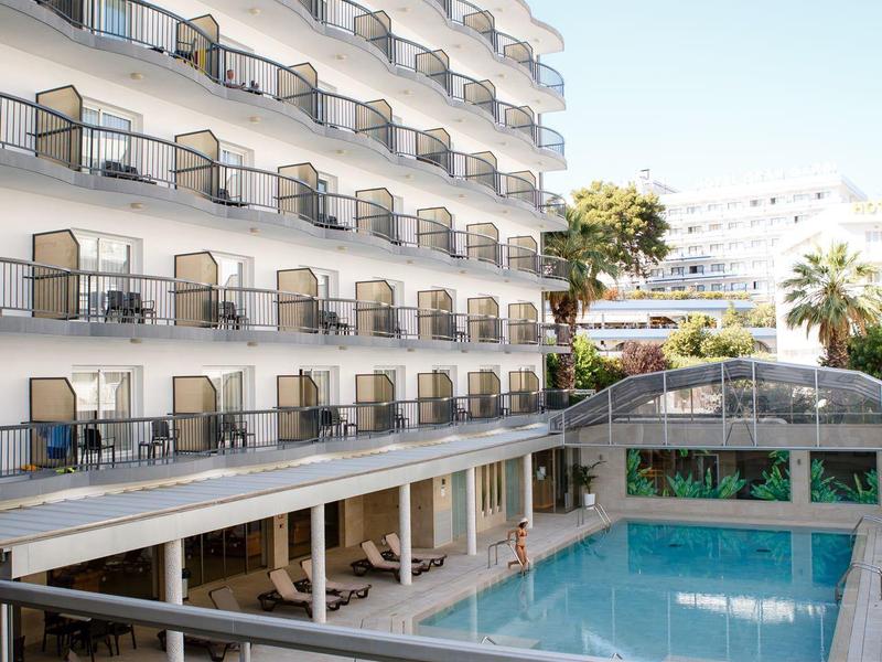 Modern hotel met balkons, buitenzwembad, ligstoelen en heldere blauwe lucht.