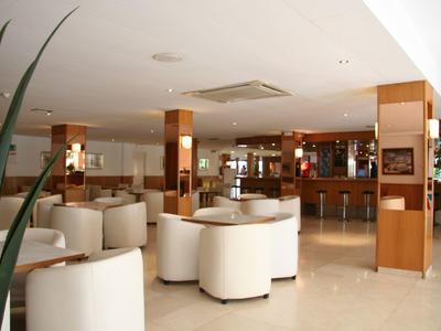 Große helle Hotelbar mit runden weißen Sesseln, Holzwänden und barrierefreier Theke.