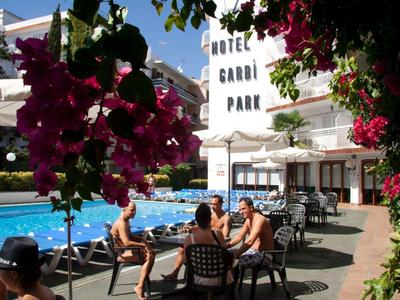 Jardin d'hôtel avec piscine, clients aux tables et fleurs colorées au premier plan