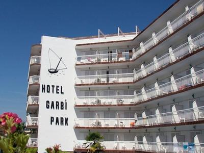 Bâtiment d'hôtel avec plusieurs balcons, piscine et chaises longues sous un ciel clair.