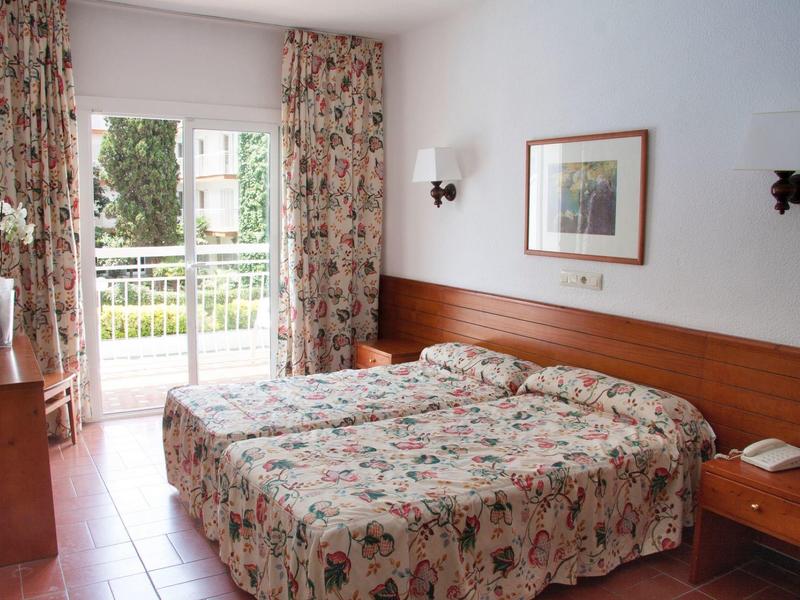 Chambre d'hôtel lumineuse avec lit double, rideaux floraux et accès au balcon.