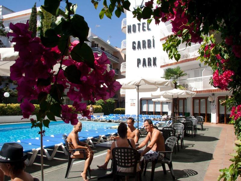 Jardin d'hôtel avec piscine, clients aux tables et fleurs colorées au premier plan