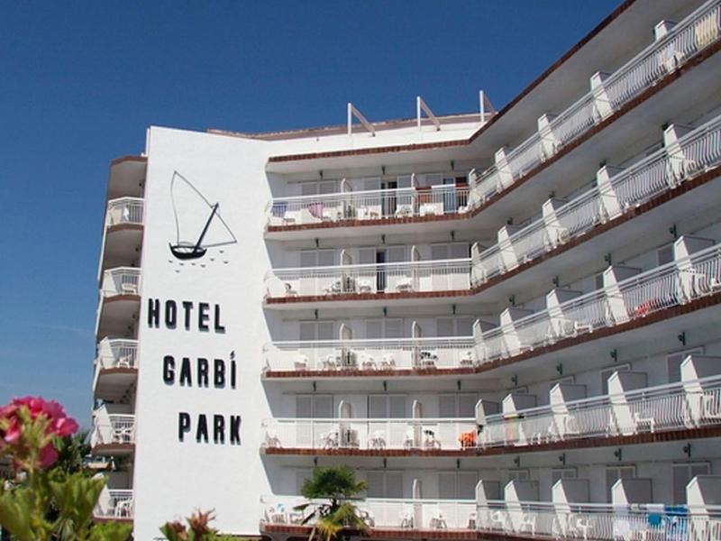 Bâtiment d'hôtel avec plusieurs balcons, piscine et chaises longues sous un ciel clair.