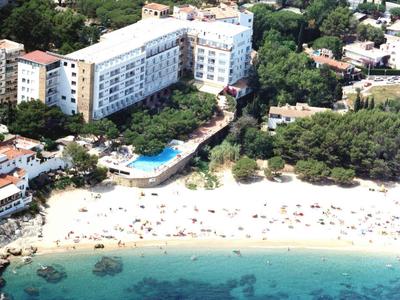 Hotel met zwembad aan een wit zandstrand en helder turquoise water, omgeven door bomen.