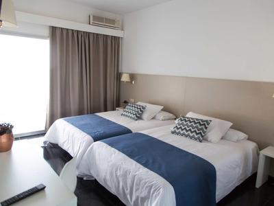 Lichte tweepersoonskamer met twee bedden, blauwe dekens en balkon toegang.