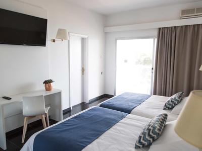 Lichte hotelkamer met twee bedden, bureau, stoel, tv en groot raam met gordijnen.