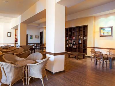 Lichte hotel lobby met rotan stoelen, houten meubels en boekenplank.