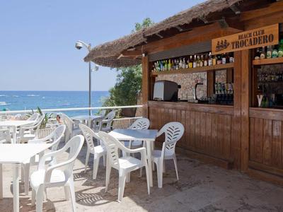 Strandbar met houten toonbank en witte kunststof stoelen met uitzicht op de zee.