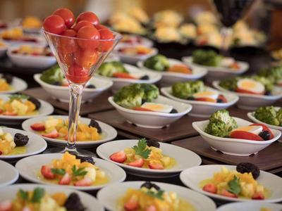 Verscheidenheid aan kleine hapjes en salades op witte borden bij een buffet.