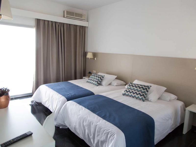 Lichte tweepersoonskamer met twee bedden, blauwe dekens en balkon toegang.