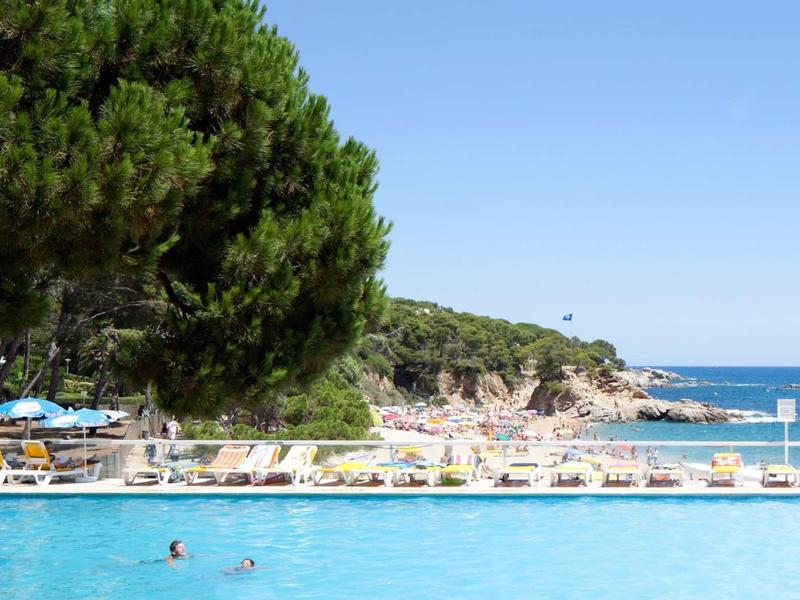 Zwembad met ligstoelen en parasols bij de zee onder een blauwe lucht