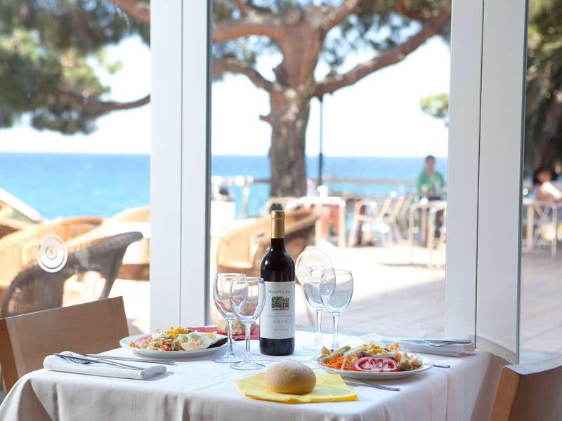 Een tafel gedekt met wijn, brood en salade voor grote ramen met uitzicht op zee.