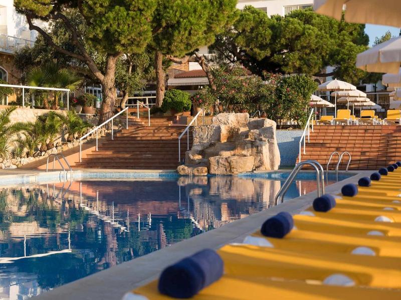 Zwembadgebied met gele ligbedden en blauwe handdoeken, omringd door bomen en trappen.