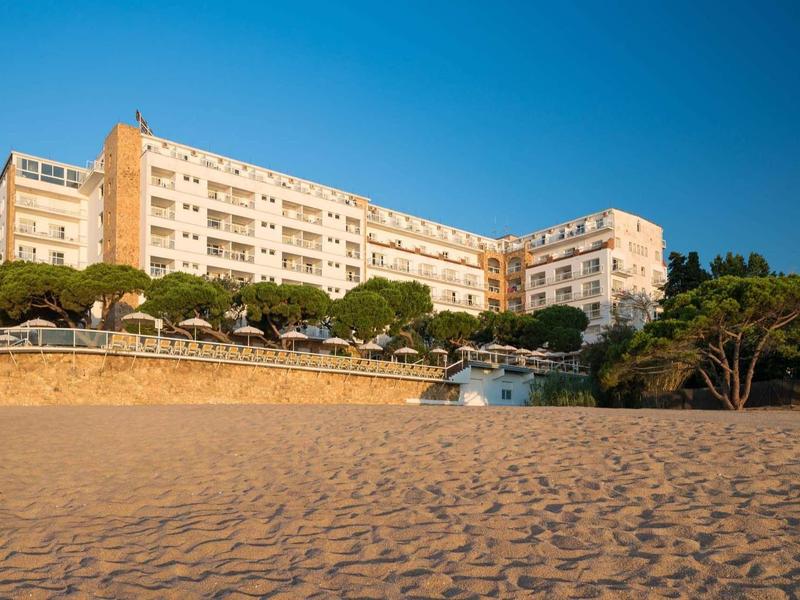 Groot hotelgebouw bij het strand onder een heldere lucht en zonneschijn.
