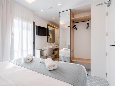 Moderní hotelový pokoj s postelí, srolovanými ručníky, otevřenou skříní a viditelnou koupelnou.