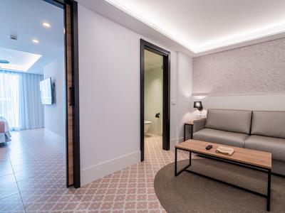 Hotelový obývací pokoj se šedou pohovkou, stolkem a světlou chodbou do pokoje.