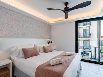 Moderní pokoj s manželskou postelí, stropním ventilátorem a světlým balkonem.