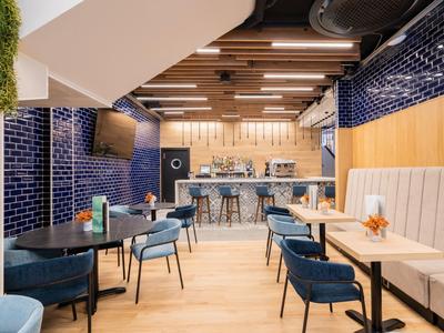 Moderní jídelna s modrými židlemi, modrými dlaždicemi na zdech a dřevěným stropem.