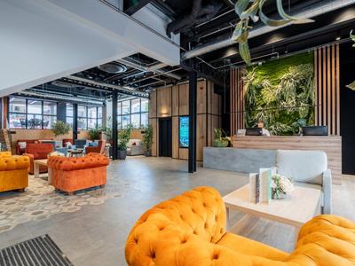 Prosvětlený lounge prostor s oranžovými pohovkami a dekorativní zelenou stěnou.