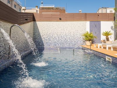 Moderner Außenpool mit Wasserfontänen und Liegestühlen an einer sonnigen Terrasse.
