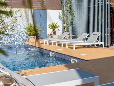 Venkovní bazén s bílými lehátky a okolní vegetací.