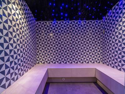 Hotelová odpočívárna s lavicemi a stěnami s geometrickými vzory pod modrým světlem.