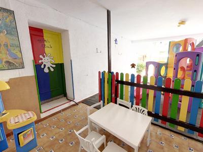 Kinderspielbereich mit buntem Zaun und Plastikküche in einem hellen Raum mit Tischen und Stühlen.