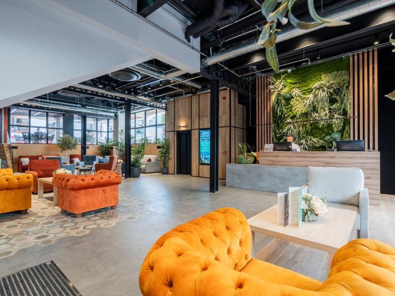 Prosvětlený lounge prostor s oranžovými pohovkami a dekorativní zelenou stěnou.