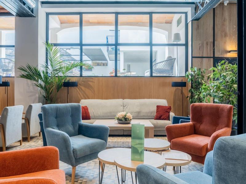 Světlý obývací pokoj s barevnými křesly, kulatými stolky, velkými okny a dekorativními rostlinami.