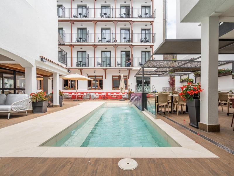 Moderní bazén obklopený lehátky na hotelovém dvoře.