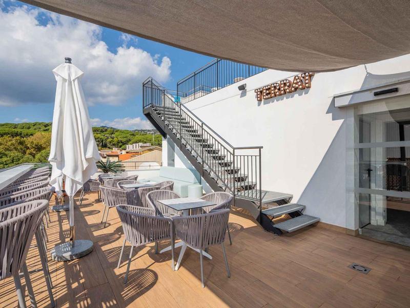 Hotelová terasa s stolky, židlemi a slunečníky pod částečně zataženou oblohou.