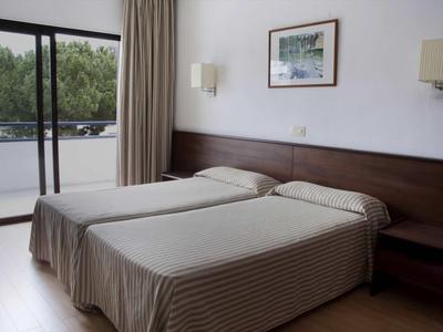 Schlichtes Schlafzimmer mit zwei Betten, braunen Kopfteil, weißen Wänden und Balkon mit Blick ins Grüne.