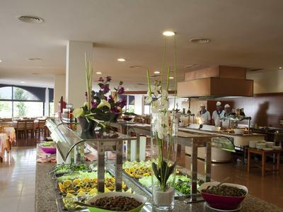 Großer, heller Gastraum mit Buffet, Tischen, Stühlen und Blumendekoration auf dem Tresen.