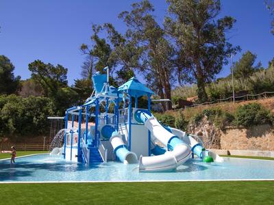 Wasser-Spielplatz mit blauen Rutschen und Klettergerüsten in flachem Pool vor Bäumen.