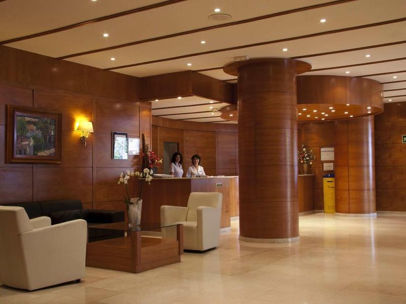 Hall d'hotel con pareti in legno, poltrone bianche e reception con personale.